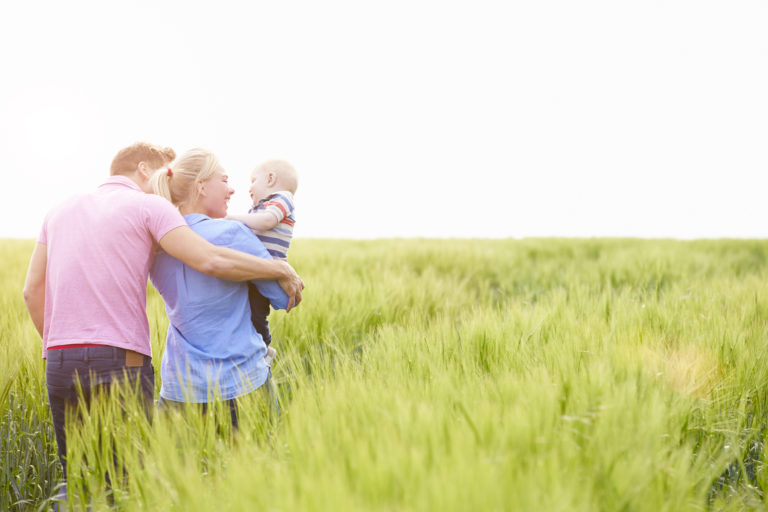 Family Walking In Field Carrying Young Baby Son